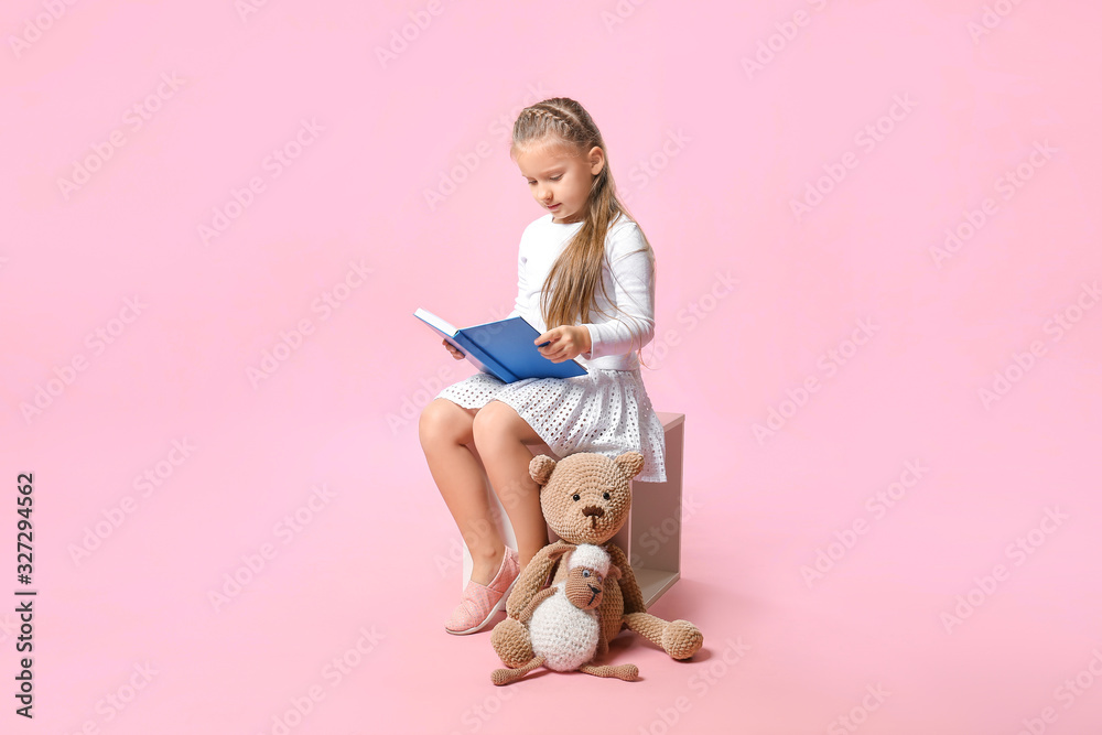 Cute little girl reading book on color background