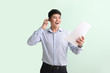 © Pixel-Shot - Happy young Asian businessman with mobile phone and documents on color background