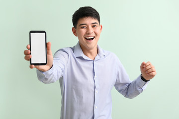 Poster - Happy young Asian businessman with mobile phone on color background