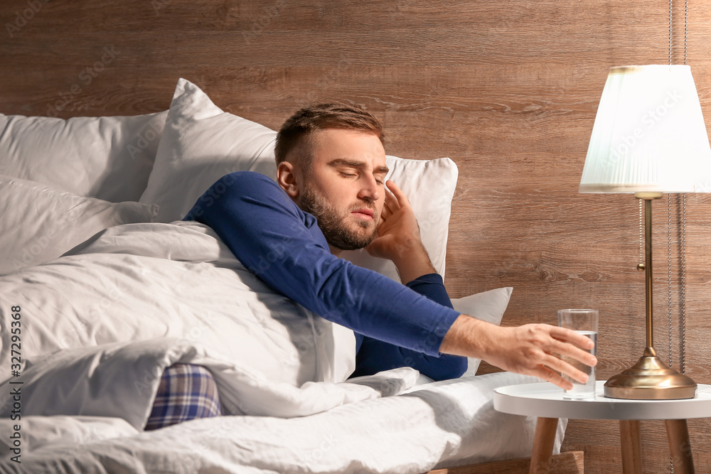 Young man taking glass of water from bedside table at night