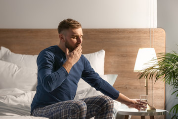 Poster - Young man taking glass of water from bedside table at night