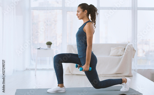 Fotografía Slim Hispanic girl doing lunges with dumbbells at home, empty space