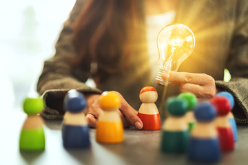 Wall Mural - closeup image of a woman holding and putting a light bulb over one of a different colors wooden peop