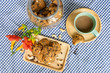 chocolate chip and nuts cookies decorated on a wooden plate with a cup of coffee, a cookie jar and flowers on a blue and white checked table cloth shot from above