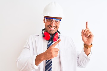 Wall Mural - Young chemist man wearing security helmet and headphones over isolated background smiling and looking at the camera pointing with two hands and fingers to the side.