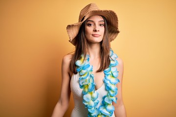 Wall Mural - Young beautiful brunette woman on vacation wearing swimsuit and Hawaiian flowers lei with serious expression on face. Simple and natural looking at the camera.