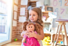 Adorable Blonde Toddler Hugigng Doll Around Lots Of Toys At Kindergarten