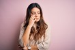 Young beautiful brunette woman wearing casual sweater standing over pink background looking stressed and nervous with hands on mouth biting nails. Anxiety problem.