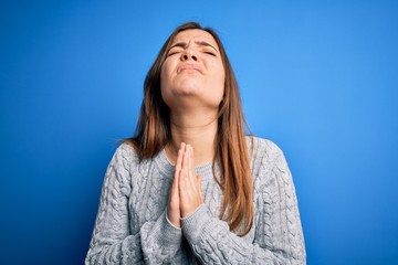 Sticker - Beautiful young woman wearing casual wool sweater standing over blue isolated background begging and praying with hands together with hope expression on face very emotional and worried. Begging.