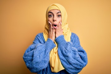 Wall Mural - Young beautiful brunette muslim woman wearing arab hijab over isolated yellow background afraid and shocked, surprise and amazed expression with hands on face