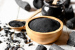 Black charcoal powder for facial mask and scrub, placed on a white wooden table, health and beauty concept.