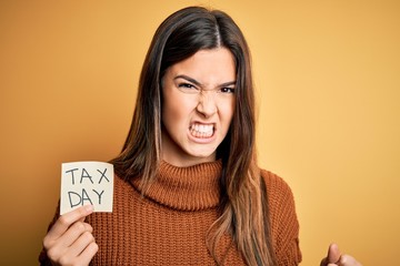 Sticker - Young beautiful girl holding reminder paper with tax day message over yellow background annoyed and frustrated shouting with anger, crazy and yelling with raised hand, anger concept