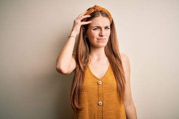 Young beautiful redhead woman wearing casual t-shirt and diadem over yellow background confuse and wonder about question. Uncertain with doubt, thinking with hand on head. Pensive concept.