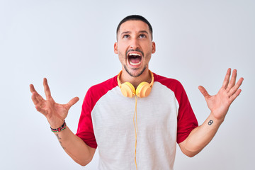 Poster - Young handsome man wearing headphones over isolated background crazy and mad shouting and yelling with aggressive expression and arms raised. Frustration concept.