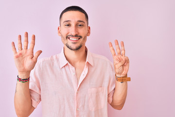 Wall Mural - Young handsome man wearing pink shirt standing over isolated background showing and pointing up with fingers number eight while smiling confident and happy.