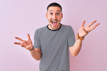 Canvas Print - Young handsome man wearing striped t-shirt standing over pink isolated background celebrating crazy and amazed for success with arms raised and open eyes screaming excited. Winner concept