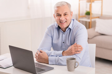 Senior man using laptop at office and looking at camera