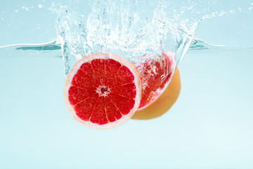Aufkleber - Halves of delicious grapefruit flowing into deep water on blue background