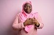 canvas print picture - Young african american plus size woman wearing muslim hijab over isolated pink background smiling with hands on chest with closed eyes and grateful gesture on face. Health concept.