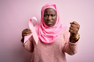 Sticker - Young african american plus size woman wearing muslim hijab holding pink cancer ribbon annoyed and frustrated shouting with anger, crazy and yelling with raised hand, anger concept