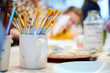canvas print picture - Bunte Pinsel mit gelben Borsten stehen in einer Kaffeetasse auf dem Tisch einer Kunstschule
