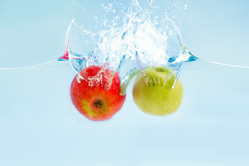 Aufkleber - Yummy green and red apples falling into water with splashes on blue background