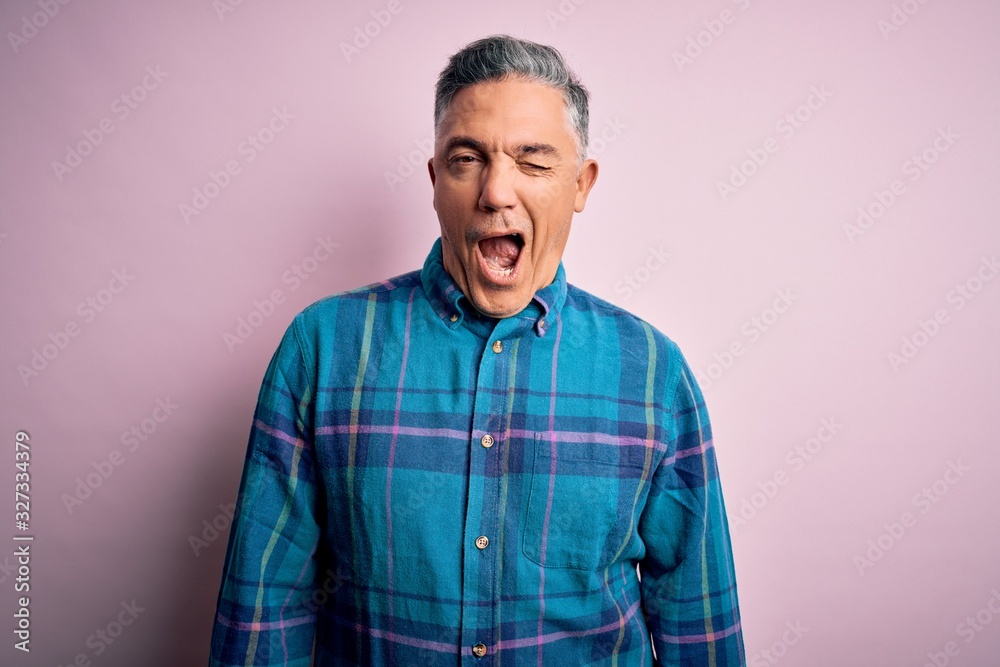Middle age handsome grey-haired man wearing casual shirt over isolated pink background winking looking at the camera with sexy expression, cheerful and happy face.