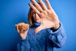 © Krakenimages.com - Young beautiful brunette woman holding bowl with peanuts over blue background with open hand doing stop sign with serious and confident expression, defense gesture