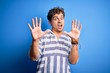 © Krakenimages.com - Young blond handsome man with curly hair wearing casual striped sweatshirt afraid and terrified with fear expression stop gesture with hands, shouting in shock. Panic concept.
