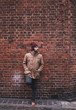 © javiemebravo - Young man with hat and warm clothes leaning against brick wall looking sideways in a London street
