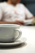 © PHILL THORNTON PHOTO - Close up shot of a white coffee cup and saucer, with an out of focus person in the background, reading a book