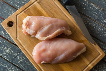 Fresh chicken meat on a wooden kitchen board and a cutting knife.