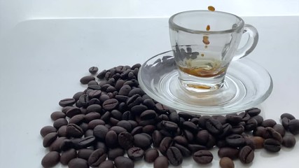 Wall Mural - slow motion pouring coffee in small glass transparent cup saucer full coffee beans 