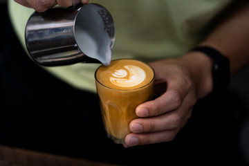 Wall Mural - Close-up of male barista hand holding and pouring hot milk for prepare latte art on piccolo latte cup of coffee.