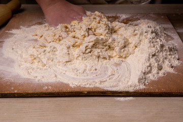 A woman kneads the dough. Plywood cutting board, wooden flour sieve and wooden rolling pin - tools for making dough.