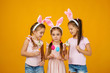 © producer - happy cute little child girls with pink bunny ears holding painted Easter eggs on studio yellow background. Easter day
