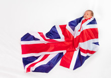 Portrait Of Little Baby Infant Boy Wrapped In UK Flag Laying On The Bed Sheet