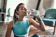 © Valerii Apetroaiei - Athletic woman in sportswear sitting on the floor and drinking water from a bottle at home in the living room. Sport and recreation concept.