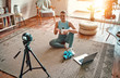Woman blogger in sportswear sitting on the floor with dumbbells and a laptop and showing a jar of sports nutrition proteins to the camera at home in the living room. Sport and recreation concept.