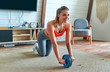 © Valerii Apetroaiei - Beautiful strong woman in sportswear is working out with exercise wheel at home in the living room. Sport and recreation concept.