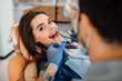 © Тарас Нагирняк - Young female patient visiting dentist office. Beautiful woman with healthy straight white teeth sitting at dental chair with open mouth during oral checkup while doctor working at teeth.