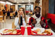 © Тарас Нагирняк - Two students having fun during lunch at bar, sitting at table with drinks and fast food.