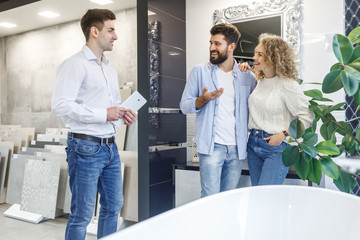 Wall Mural - Portrait of happy couple standing with assistant near new bath in the modern shop