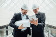 © Тарас Нагирняк - Two young businesssmen or construction worker in helmet stands in white building, holding a sheet of paper, projecting.