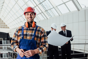 Worker with red helmet and jeans shirt near a industrial  fabric wall.