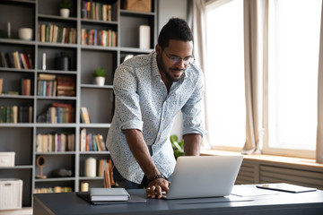 Wall Mural - Happy young biracial freelance man working standing at table.