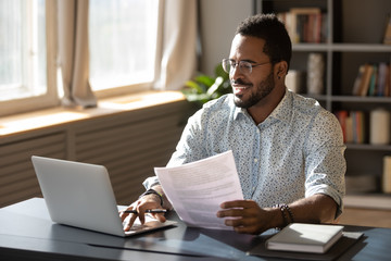 happy millennial african american businessman in eyewear doing paperwork.