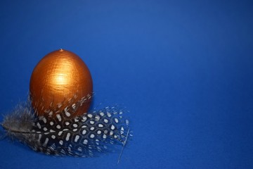 Wall Mural - Easter egg with black and white feather feather on a blue background.