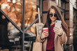 © klepach - Young pretty woman in coat with shopping bags, cup of black coffee and smartphone