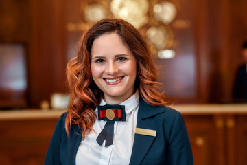 Smiling service. Close up of happy female receptionist worker in uniform looking at camera with a smile while standing at hotel lobby